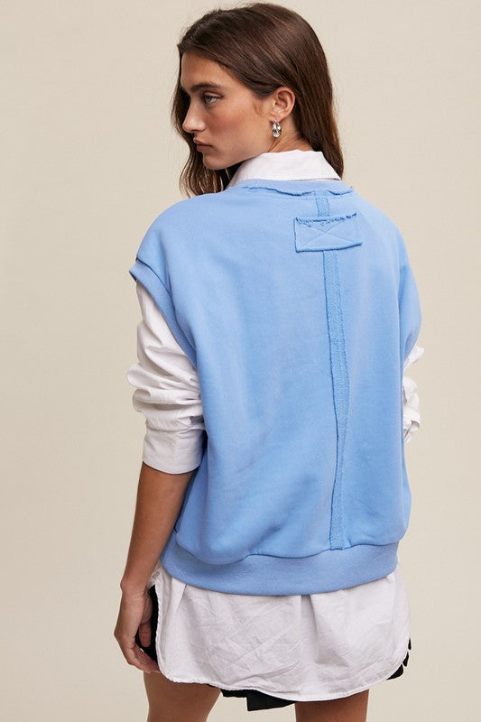 A woman stands against a neutral background, wearing the Short Sleeve Boxy Crew Neck Sweat Top in blue with ribbed detailing over a white button-up shirt.