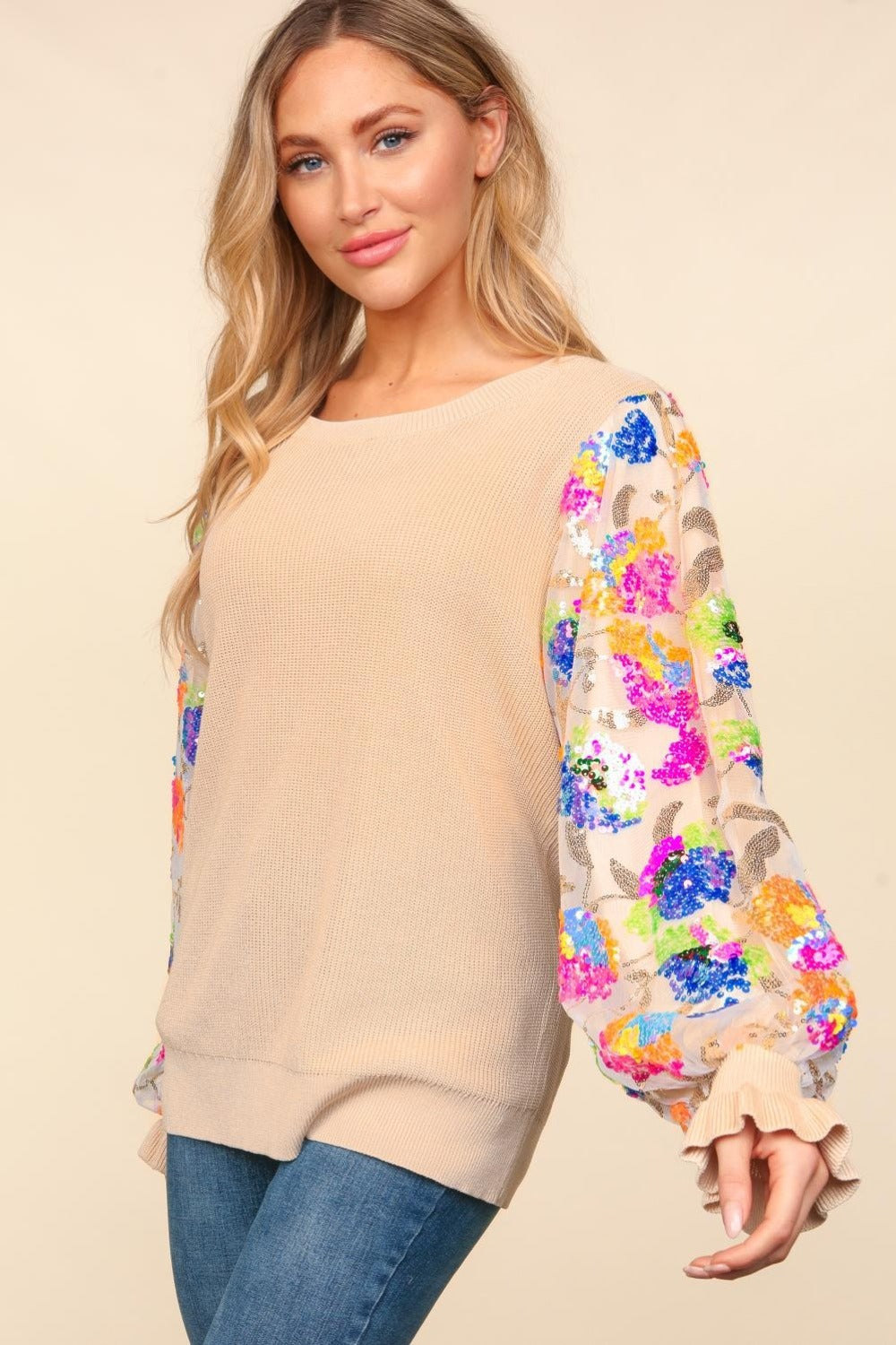 A person wearing the Haptics Floral Sequins Mesh Flounce Sleeve Sweater and blue jeans poses against a plain background.