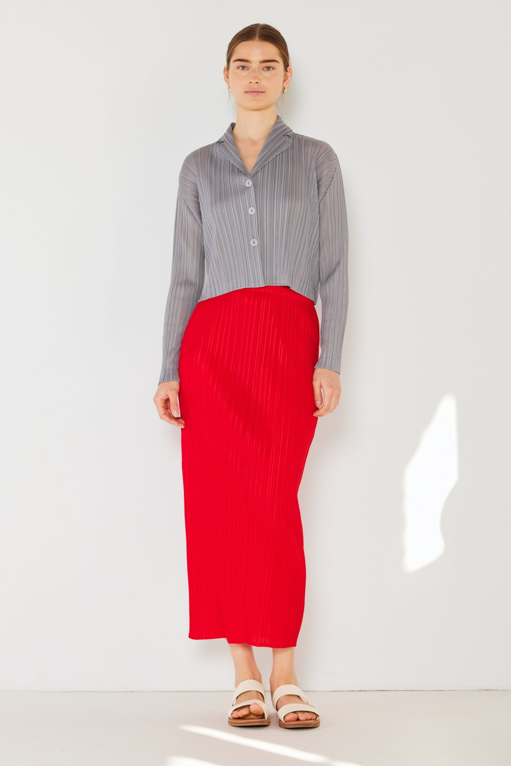 A person wearing the Marina West Swim Pleated Cropped Button Up Shirt in teal, complete with long sleeves and a matching skirt, stands against a light background, adding a modern touch to the classic pleats.