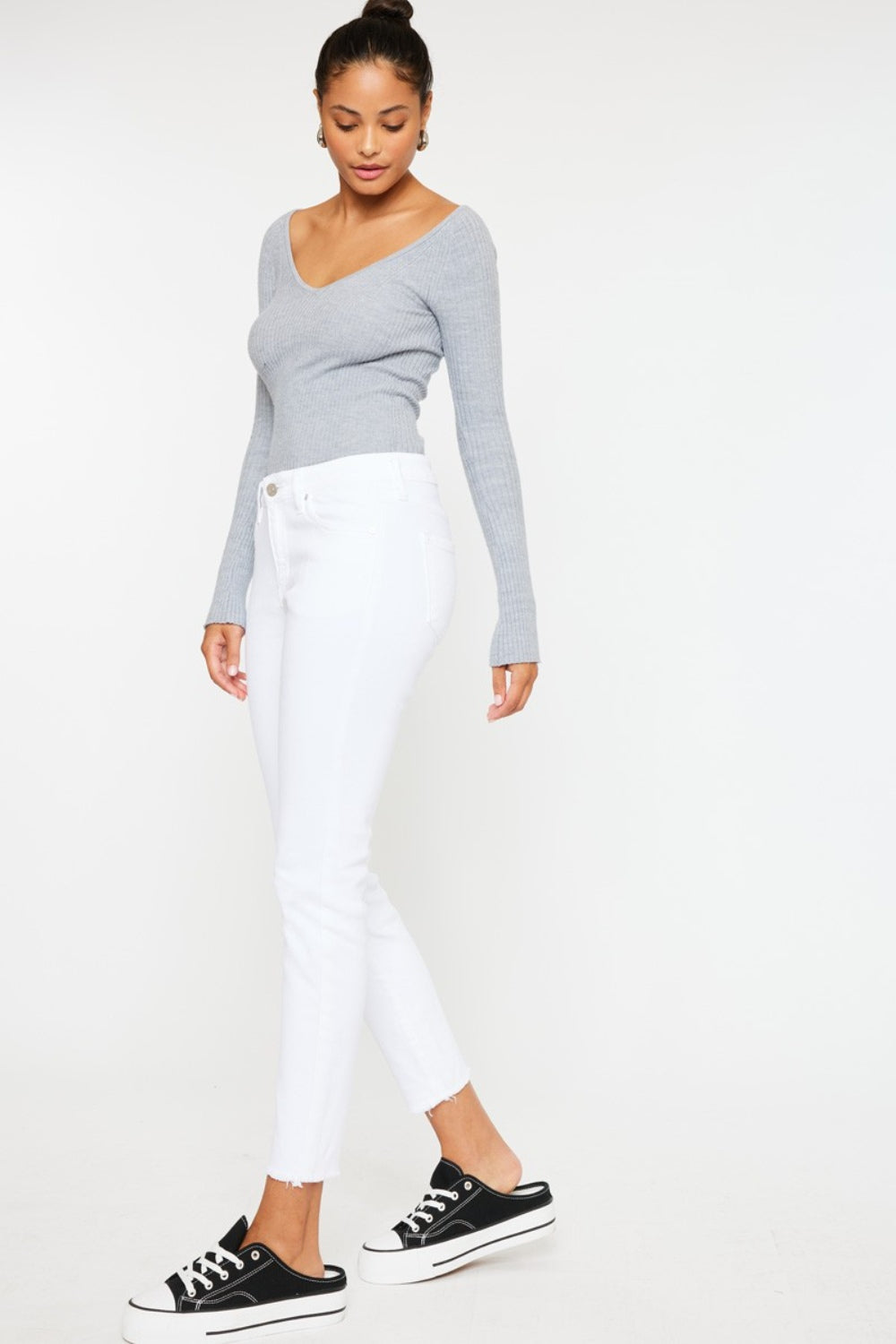 A person models a versatile gray long-sleeve top paired with flattering fit Kancan Mid Rise Ankle Skinny Jeans and sleek black sneakers, all set against a pristine white background.