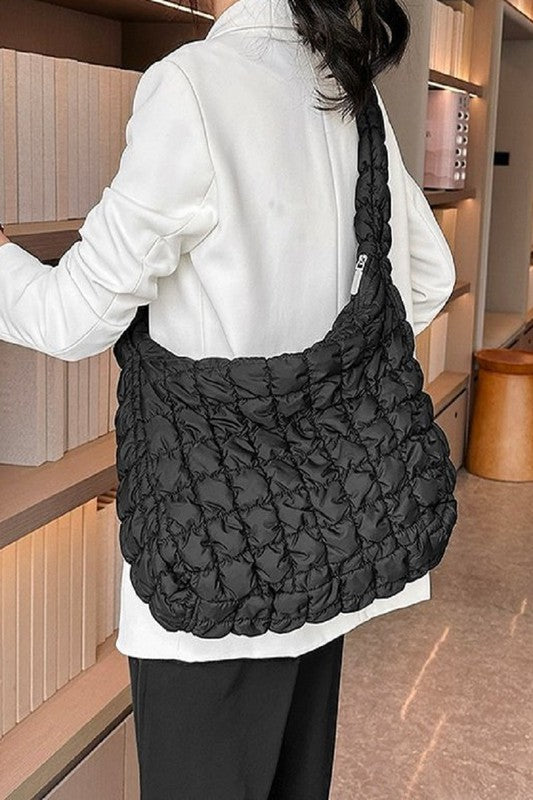 Woman in a white sweater and jeans holding a large black Puff Quilted Crossbody Shoulder Bag.