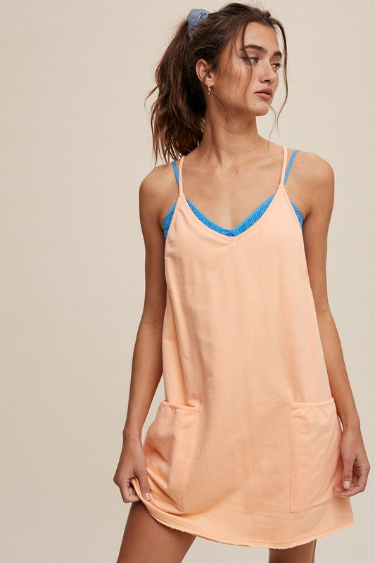 A person stands with their hands behind their head, wearing a Sporty Mini Dress With Built in Romper Liner in light blue, featuring two front pockets and a V-neckline.