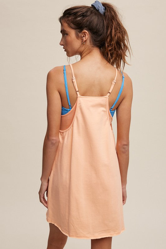 A person stands with their hands behind their head, wearing a Sporty Mini Dress With Built in Romper Liner in light blue, featuring two front pockets and a V-neckline.