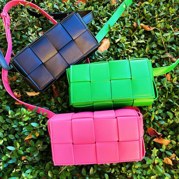 Three small Candy Cube Woven Sling Bags in green, pink, and black, made from faux leather PU material, being held by a hand against a white background.