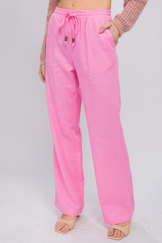 Person wearing vibrant pink Linen Drawstring Waist Long Pants with Pockets featuring a relaxed fit and a brownish sweater, standing with hands in pockets against a neutral background.