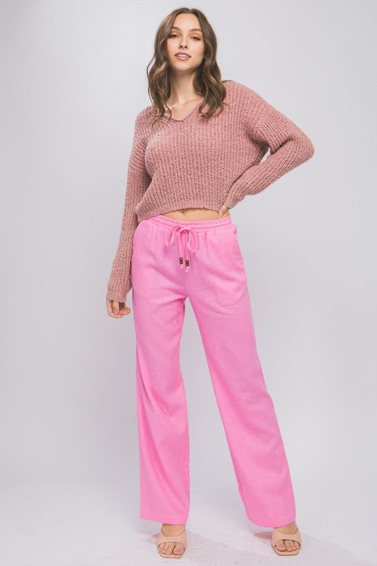 Person wearing vibrant pink Linen Drawstring Waist Long Pants with Pockets featuring a relaxed fit and a brownish sweater, standing with hands in pockets against a neutral background.