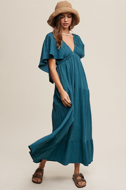 A person in a wide-brimmed hat and the V-neck Ruffle Sleeve Flowy Vacation Dress, featuring a tiered skirt and deep V-neckline, stands against a neutral background.