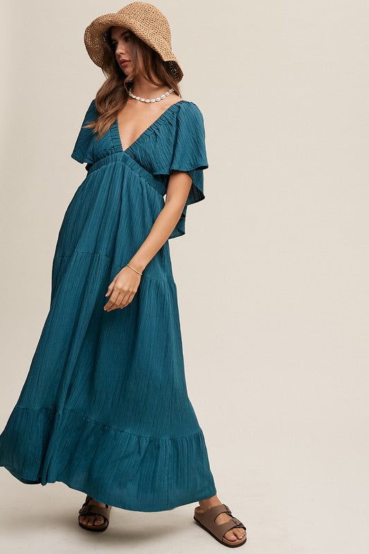 A person in a wide-brimmed hat and the V-neck Ruffle Sleeve Flowy Vacation Dress, featuring a tiered skirt and deep V-neckline, stands against a neutral background.