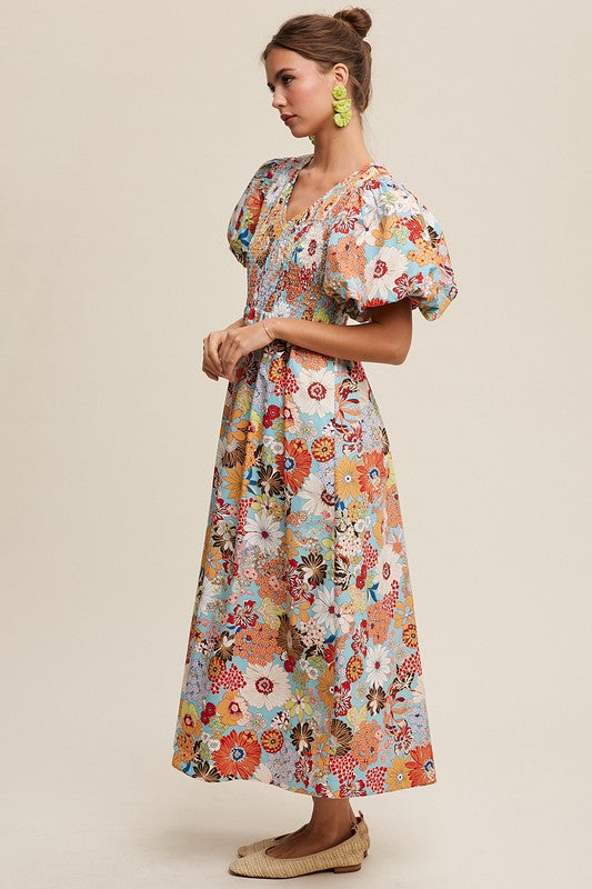 A woman in a Flower Print Smocked V-neck Puff Sleeve Maxi Dress stands gracefully against a plain background.