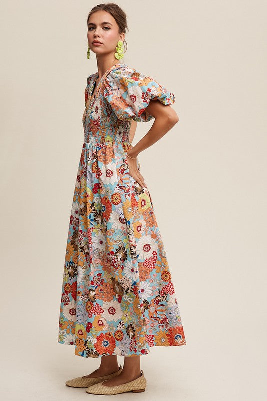 A woman in a Flower Print Smocked V-neck Puff Sleeve Maxi Dress stands gracefully against a plain background.