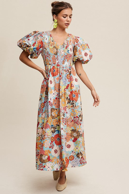 A woman in a Flower Print Smocked V-neck Puff Sleeve Maxi Dress stands gracefully against a plain background.