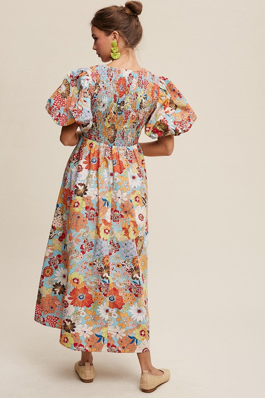 A woman in a Flower Print Smocked V-neck Puff Sleeve Maxi Dress stands gracefully against a plain background.