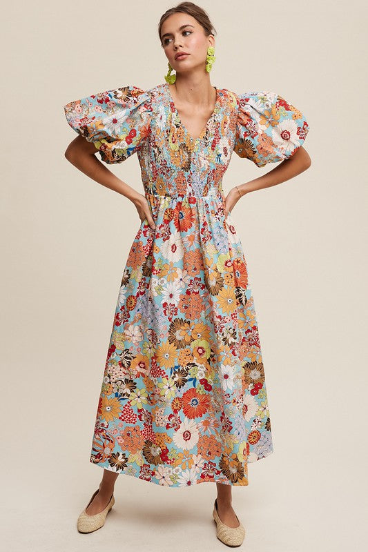 A woman in a Flower Print Smocked V-neck Puff Sleeve Maxi Dress stands gracefully against a plain background.