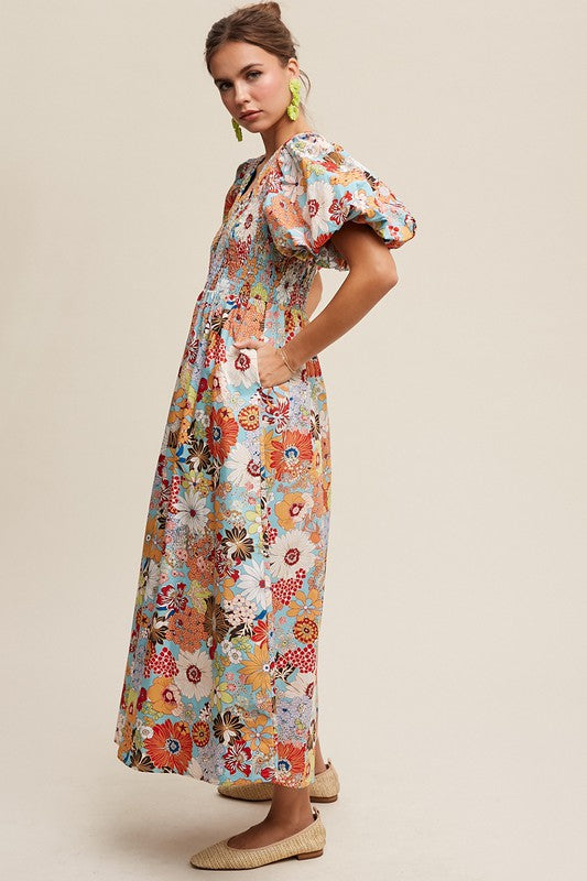 A woman in a Flower Print Smocked V-neck Puff Sleeve Maxi Dress stands gracefully against a plain background.