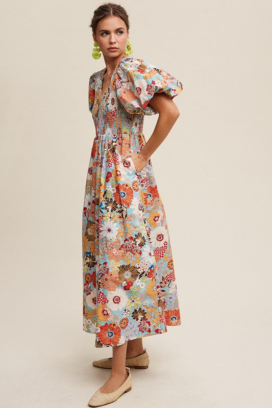 A woman in a Flower Print Smocked V-neck Puff Sleeve Maxi Dress stands gracefully against a plain background.