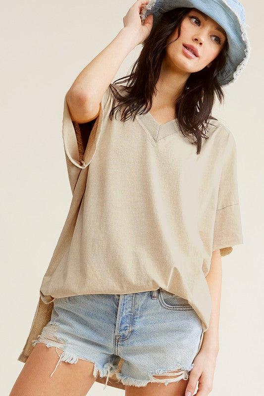 A woman wearing a Mineral Washed Oversized Short Sleeve Top, blue denim shorts, and a light blue hat, posing with hands on the hat.