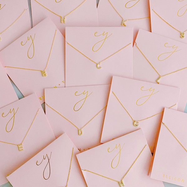 Assorted 18k gold plated Understated Beauty Initial Necklaces with various pendants, including initial necklaces and cubic zirconia embellishments, displayed in parallel lines on a light surface.