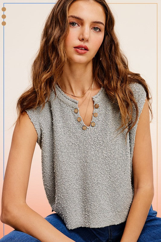 A person models a sleeveless, comfortable gray Slouchy Cropped Extended Sleeve Sweater Top with button accents against a gradient backdrop.