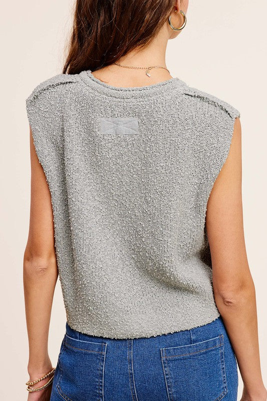 A person models a sleeveless, comfortable gray Slouchy Cropped Extended Sleeve Sweater Top with button accents against a gradient backdrop.