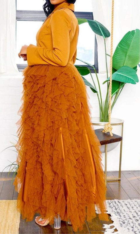 Person wearing the Noir Cascade Tuxedo Gown, which features structured shoulders, a deep V neckline, and a cascading ruffle skirt, paired with clear high-heeled shoes, exuding couture elegance.