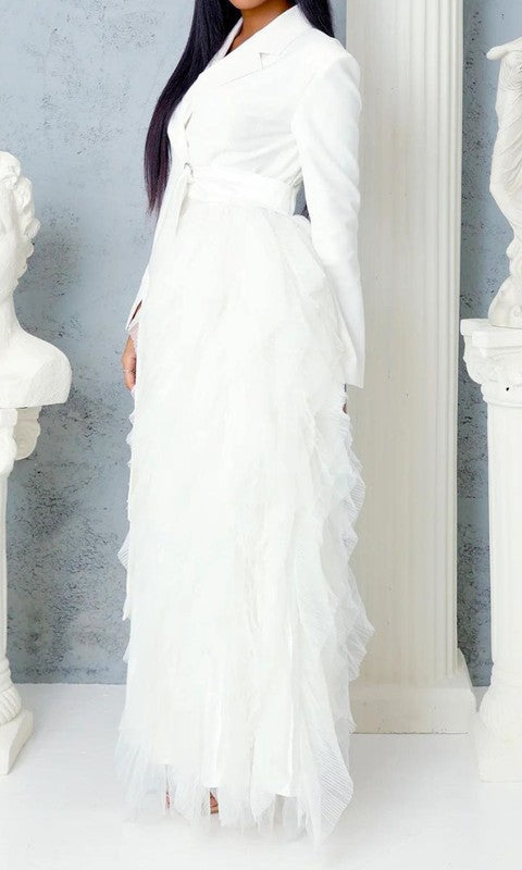 Person wearing the Noir Cascade Tuxedo Gown, which features structured shoulders, a deep V neckline, and a cascading ruffle skirt, paired with clear high-heeled shoes, exuding couture elegance.