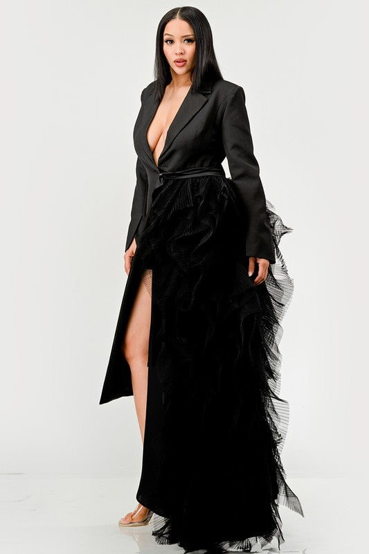 Person wearing the Noir Cascade Tuxedo Gown, which features structured shoulders, a deep V neckline, and a cascading ruffle skirt, paired with clear high-heeled shoes, exuding couture elegance.