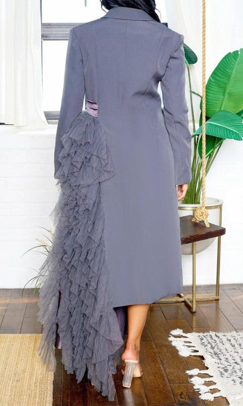 Person wearing the Noir Cascade Tuxedo Gown, which features structured shoulders, a deep V neckline, and a cascading ruffle skirt, paired with clear high-heeled shoes, exuding couture elegance.