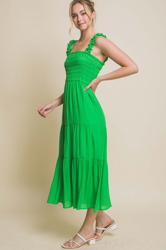 A person models the Smocked Bodice Maxi Dress, featuring a bright green hue, ruffled straps, and a sleeveless design, standing elegantly against a plain background.