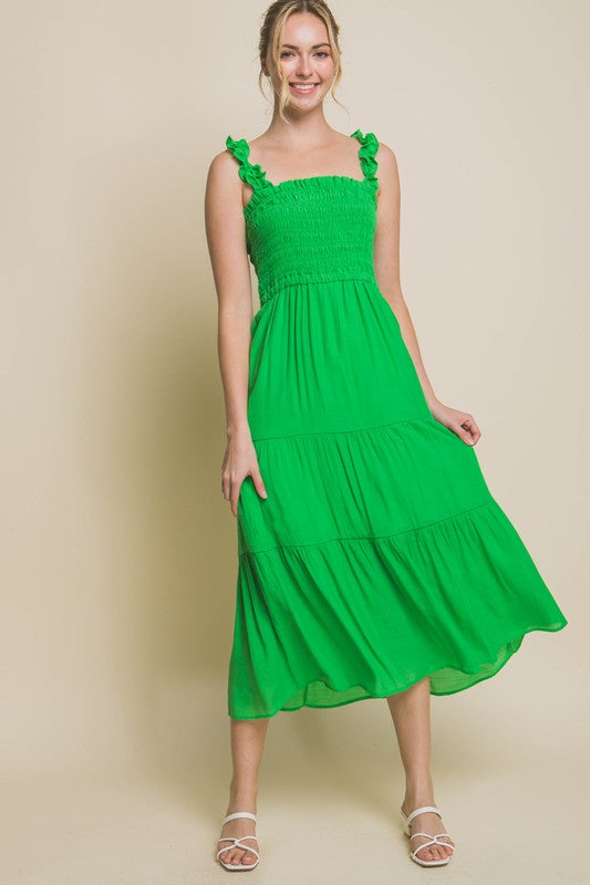 A person models the Smocked Bodice Maxi Dress, featuring a bright green hue, ruffled straps, and a sleeveless design, standing elegantly against a plain background.