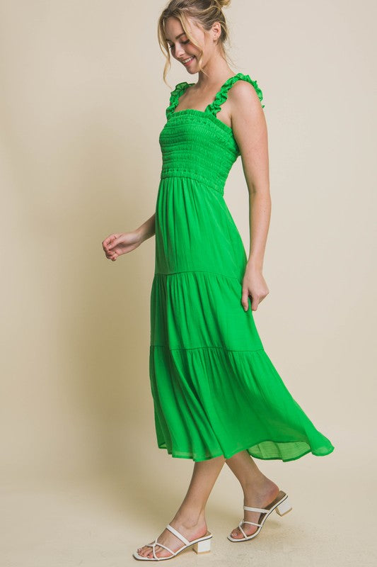 A person models the Smocked Bodice Maxi Dress, featuring a bright green hue, ruffled straps, and a sleeveless design, standing elegantly against a plain background.