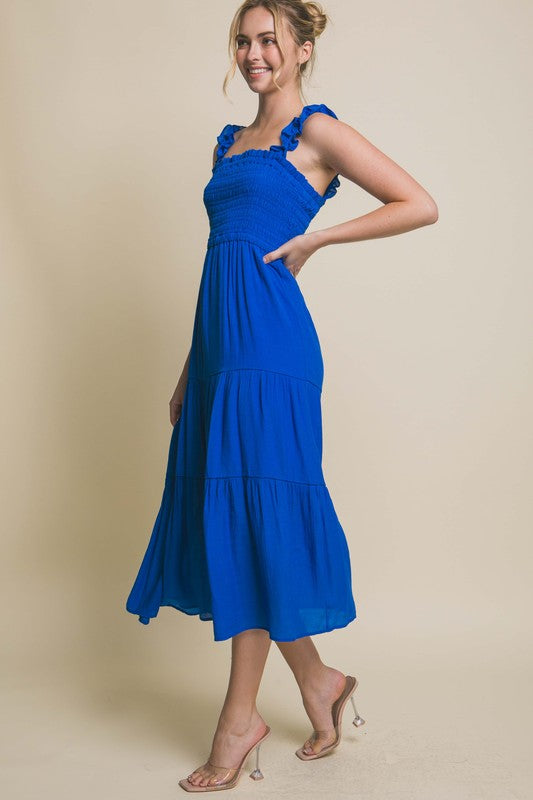 A person models the Smocked Bodice Maxi Dress, featuring a bright green hue, ruffled straps, and a sleeveless design, standing elegantly against a plain background.