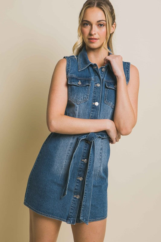 A person is wearing a strapless denim dress with a waist tie, standing against a plain backdrop.