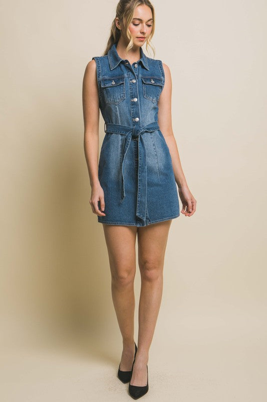 A person is wearing a strapless denim dress with a waist tie, standing against a plain backdrop.