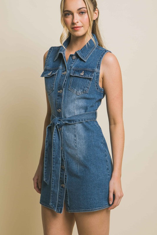 A person is wearing a strapless denim dress with a waist tie, standing against a plain backdrop.