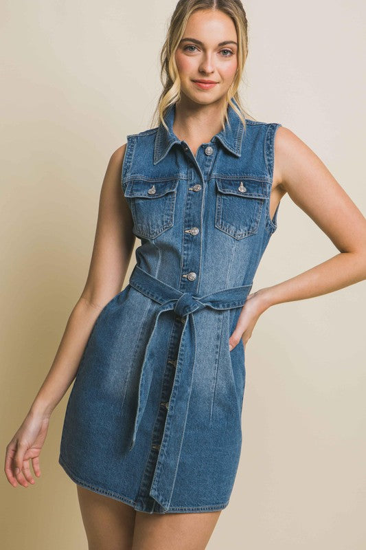 A person is wearing a strapless denim dress with a waist tie, standing against a plain backdrop.