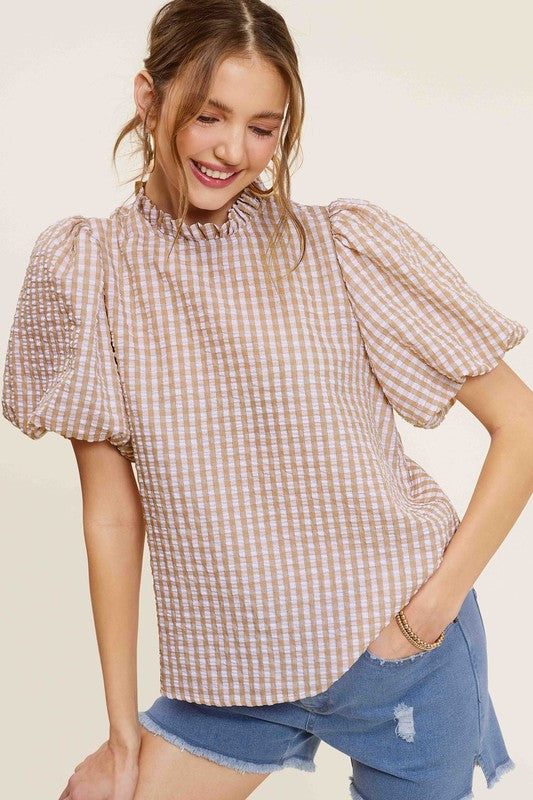 A person wearing a Gingham Check Print Puff Sleeve Top with a button-back closure sits on a chair, looking toward the camera.