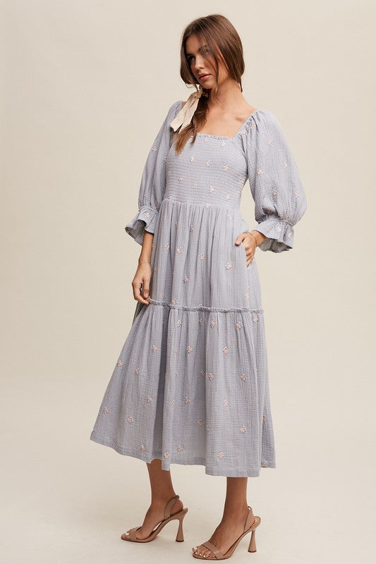 A woman is gracefully wearing the Ditzy Floral Embroidery Puff Sleeve Maxi Dress, complemented by beige shoes, as she stands against a plain background.