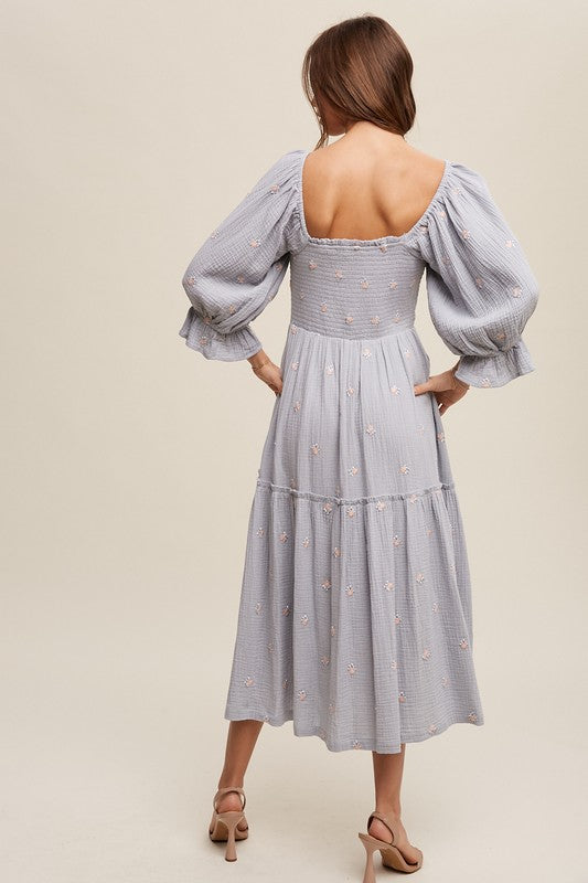 A woman is gracefully wearing the Ditzy Floral Embroidery Puff Sleeve Maxi Dress, complemented by beige shoes, as she stands against a plain background.