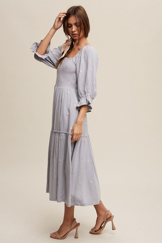 A woman is gracefully wearing the Ditzy Floral Embroidery Puff Sleeve Maxi Dress, complemented by beige shoes, as she stands against a plain background.