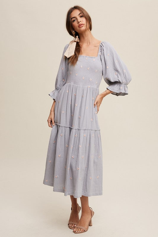 A woman is gracefully wearing the Ditzy Floral Embroidery Puff Sleeve Maxi Dress, complemented by beige shoes, as she stands against a plain background.