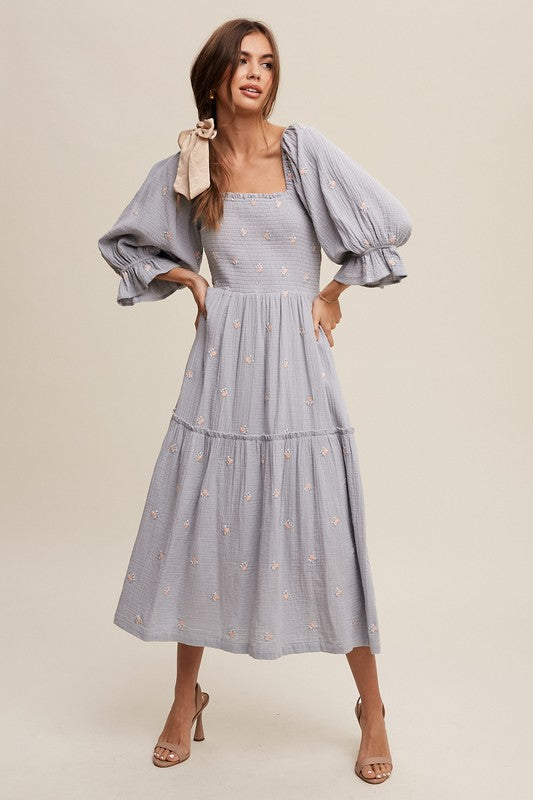 A woman is gracefully wearing the Ditzy Floral Embroidery Puff Sleeve Maxi Dress, complemented by beige shoes, as she stands against a plain background.