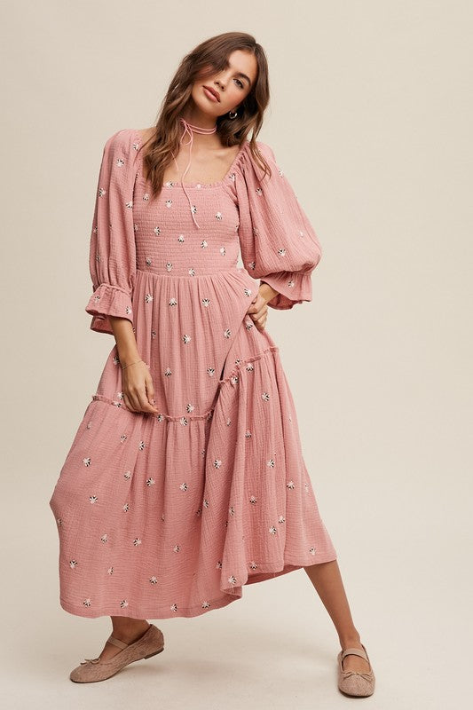 A woman is gracefully wearing the Ditzy Floral Embroidery Puff Sleeve Maxi Dress, complemented by beige shoes, as she stands against a plain background.