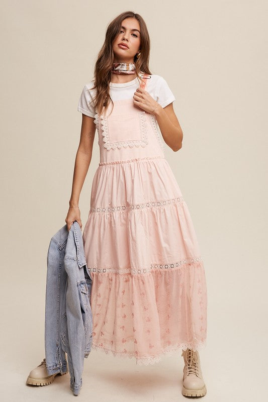 A person wearing the Laced and Tiered Romantic Overall Maxi Dress, complemented by a straw hat and brown sandals, stands gracefully against a plain background.