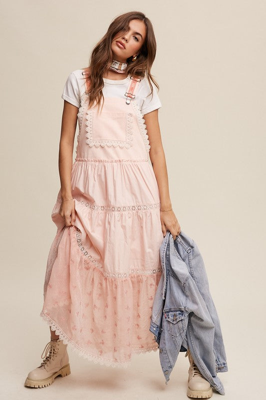 A person wearing the Laced and Tiered Romantic Overall Maxi Dress, complemented by a straw hat and brown sandals, stands gracefully against a plain background.