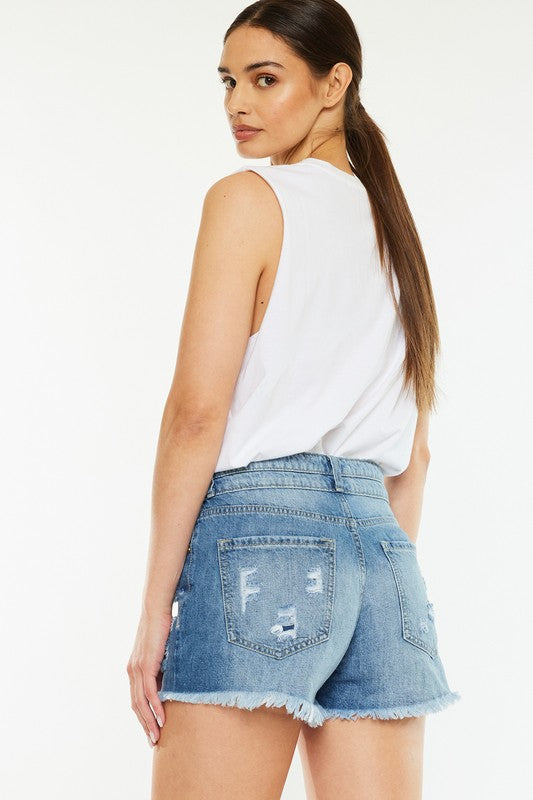 A person wearing a white sleeveless shirt, High Rise Mom Shorts in stone wash denim, and black-and-white sneakers stands against a plain background.