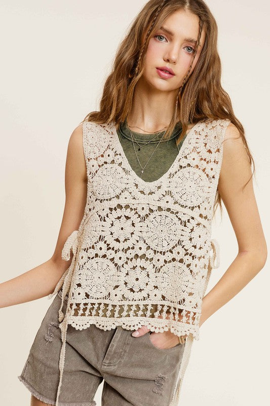 A woman wearing a Self Side Tie Detailed Crochet Vest Top paired with brown pants stands against a light background adorned with falling leaves.