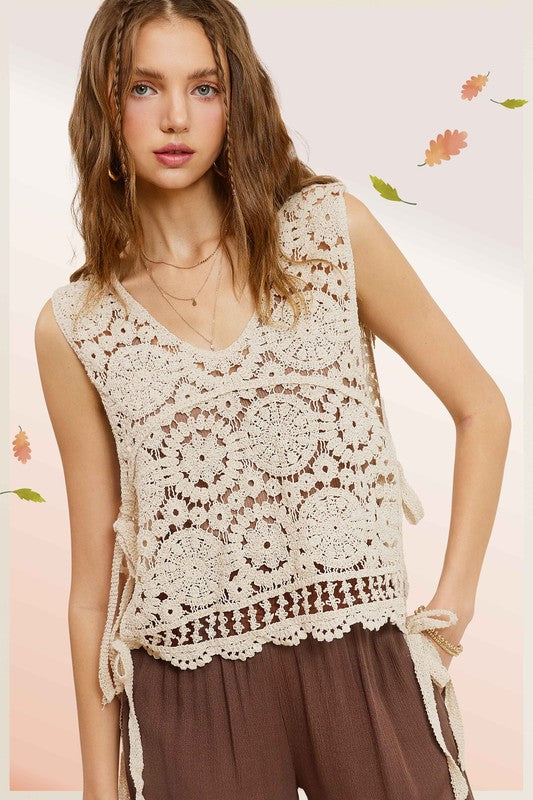 A woman wearing a Self Side Tie Detailed Crochet Vest Top paired with brown pants stands against a light background adorned with falling leaves.