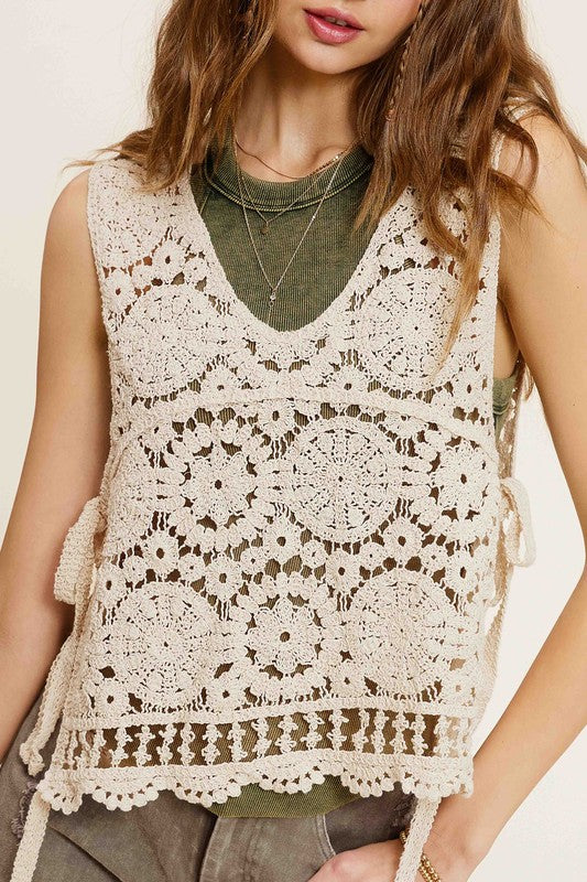 A woman wearing a Self Side Tie Detailed Crochet Vest Top paired with brown pants stands against a light background adorned with falling leaves.