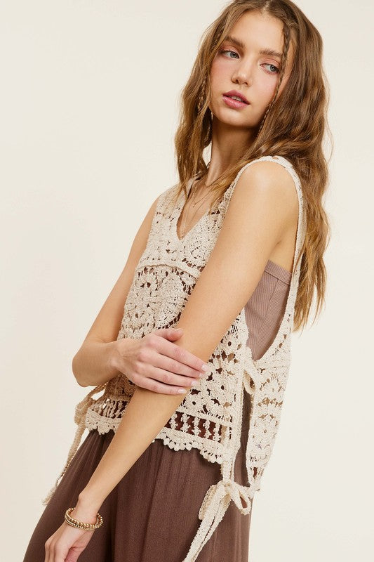 A woman wearing a Self Side Tie Detailed Crochet Vest Top paired with brown pants stands against a light background adorned with falling leaves.