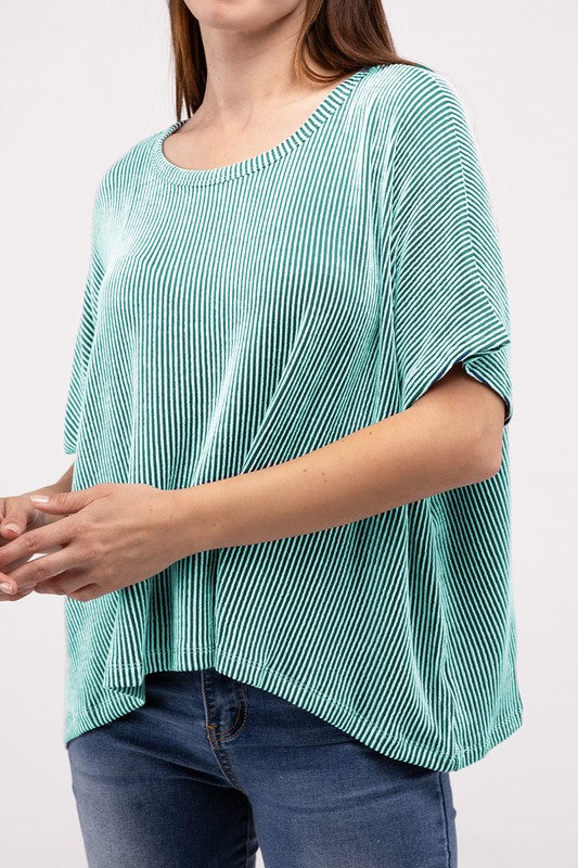 Woman wearing an oversized, short-sleeve Ribbed Striped Top in green and blue jeans, standing with her hands in her pockets against a plain background.